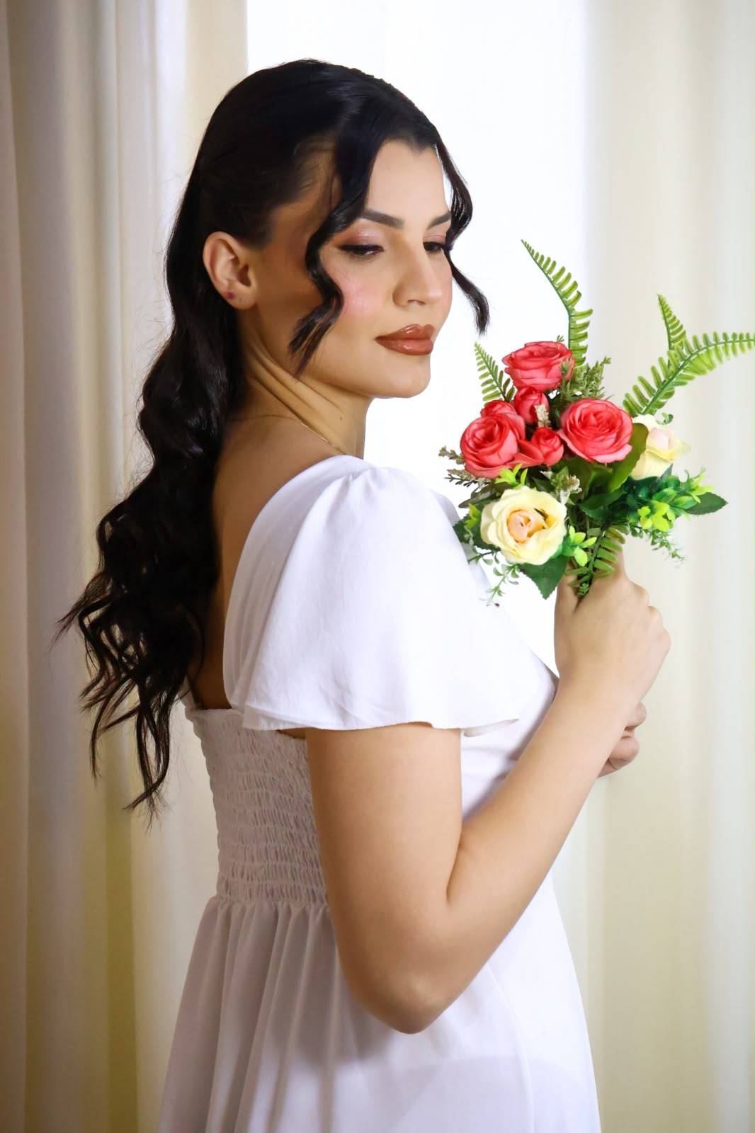 Noiva de perfil segurando o buquê, com penteado em ondas suaves